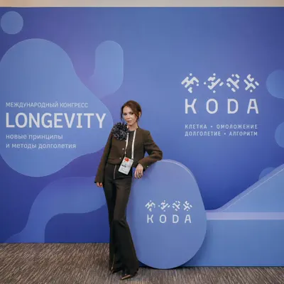Участница конгресса у синего пресс-волла с надписью Longevity