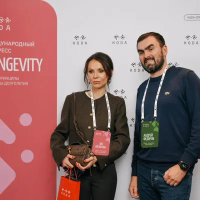 Двое участников с бейджами у брендированного пресс-волла конгресса